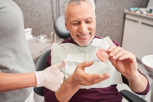 A senior man holding and looking at a denture