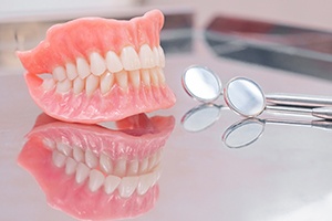 Two dentures sitting on a glass countertop next to dental tools